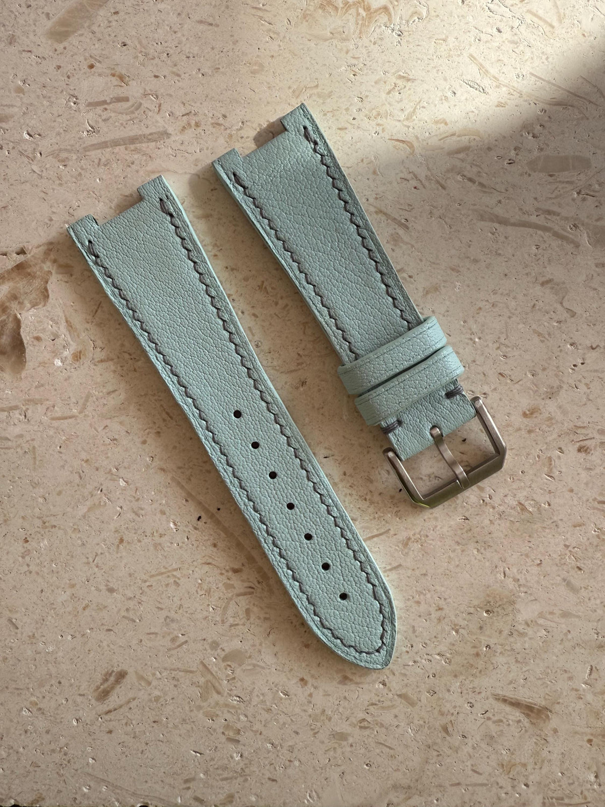 Handmade light blue goat leather watch strap laid flat, showing the long side with holes and the short side with the buckle