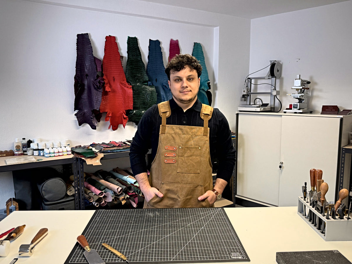 Taha at the workbench in the Atelier Taha workshop, leather hides on the wall