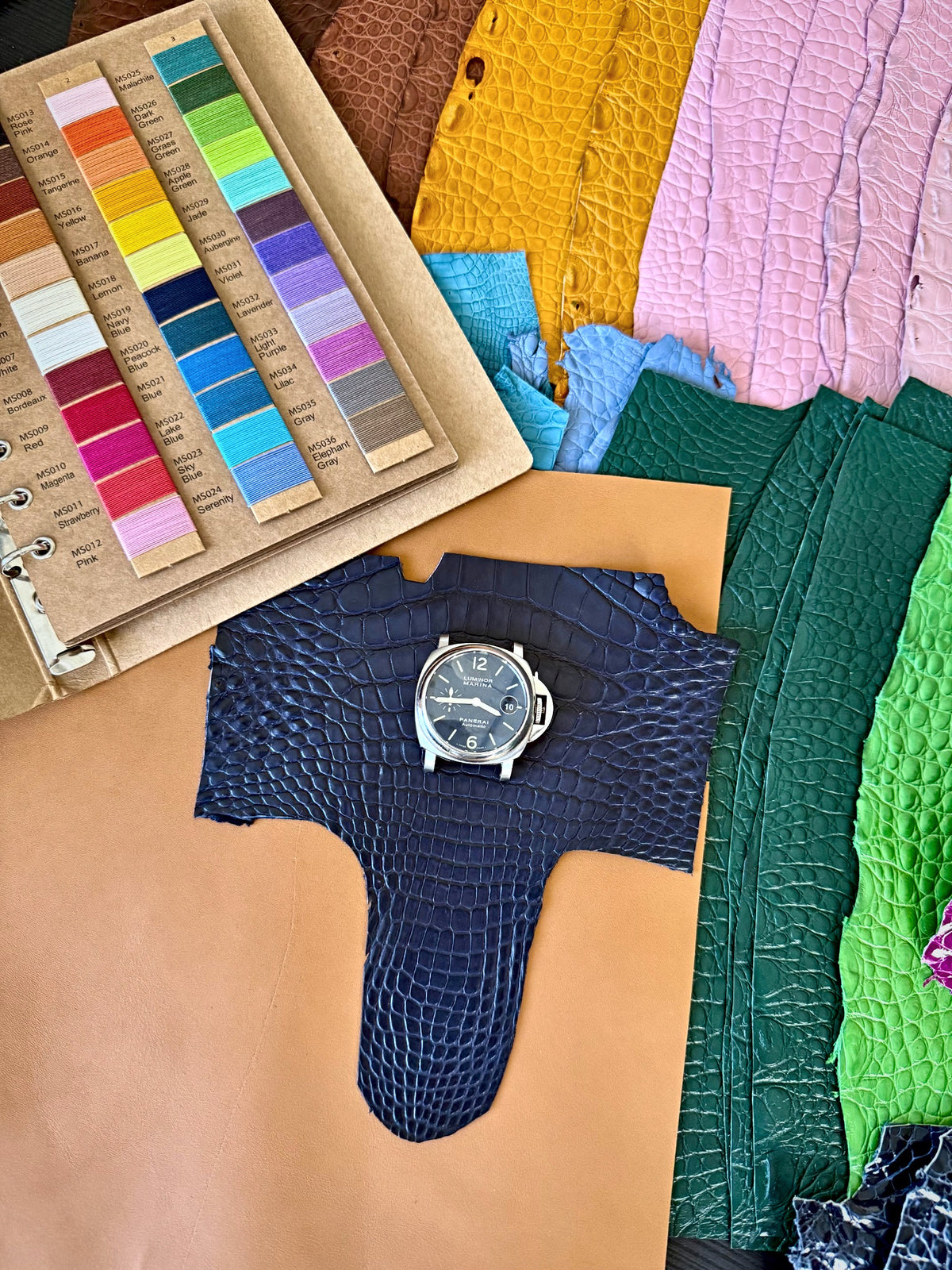 Alligator skins and colour cards around a watch on a navy alligator hide