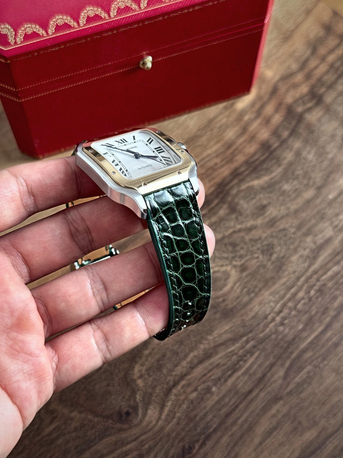 Green alligator strap on a Cartier Santos, held in the hand