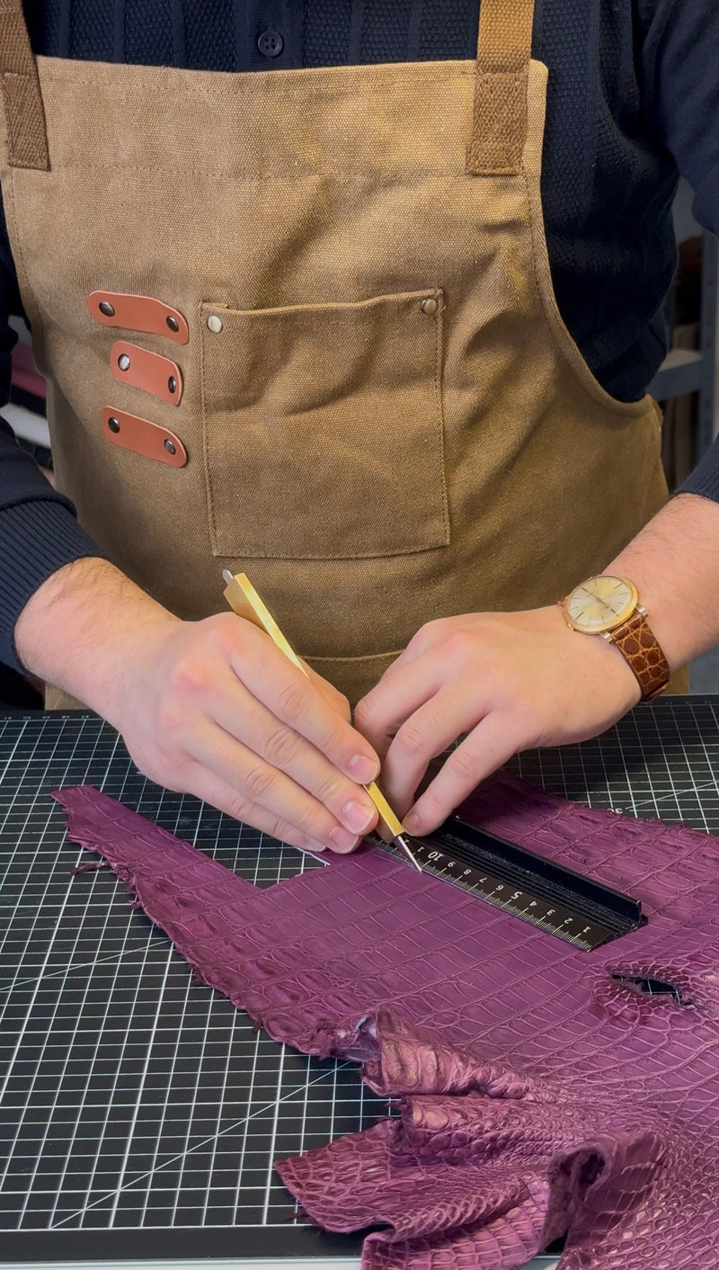 Taha schneidet ein violettes Alligatorleder von Hand an der Werkbank zu